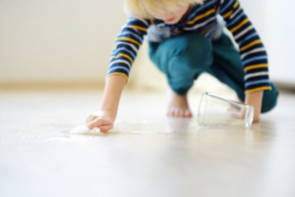 Little boy wipes water spilled from a glass on the floor