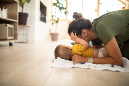 Young Mother tickling her little baby boy on floor, baby laughing