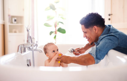 Father washing small toddler son in a bathroom indoors at home.