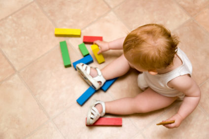Overhead view of a baby playing with colored blocks on the floor.