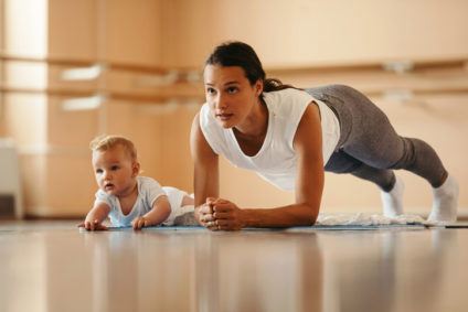 Athletic mother exercising in plank position while being with her baby in a health club