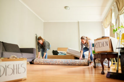 Female friends unrolling a carpet in their new home on moving day