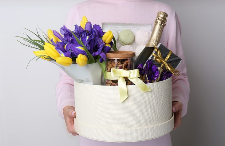 Woman holding basket with gifts, bouquet and champagne