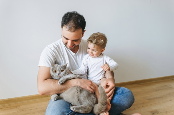father holding little son in bodysuit and grey british shorthair cat in hands at home